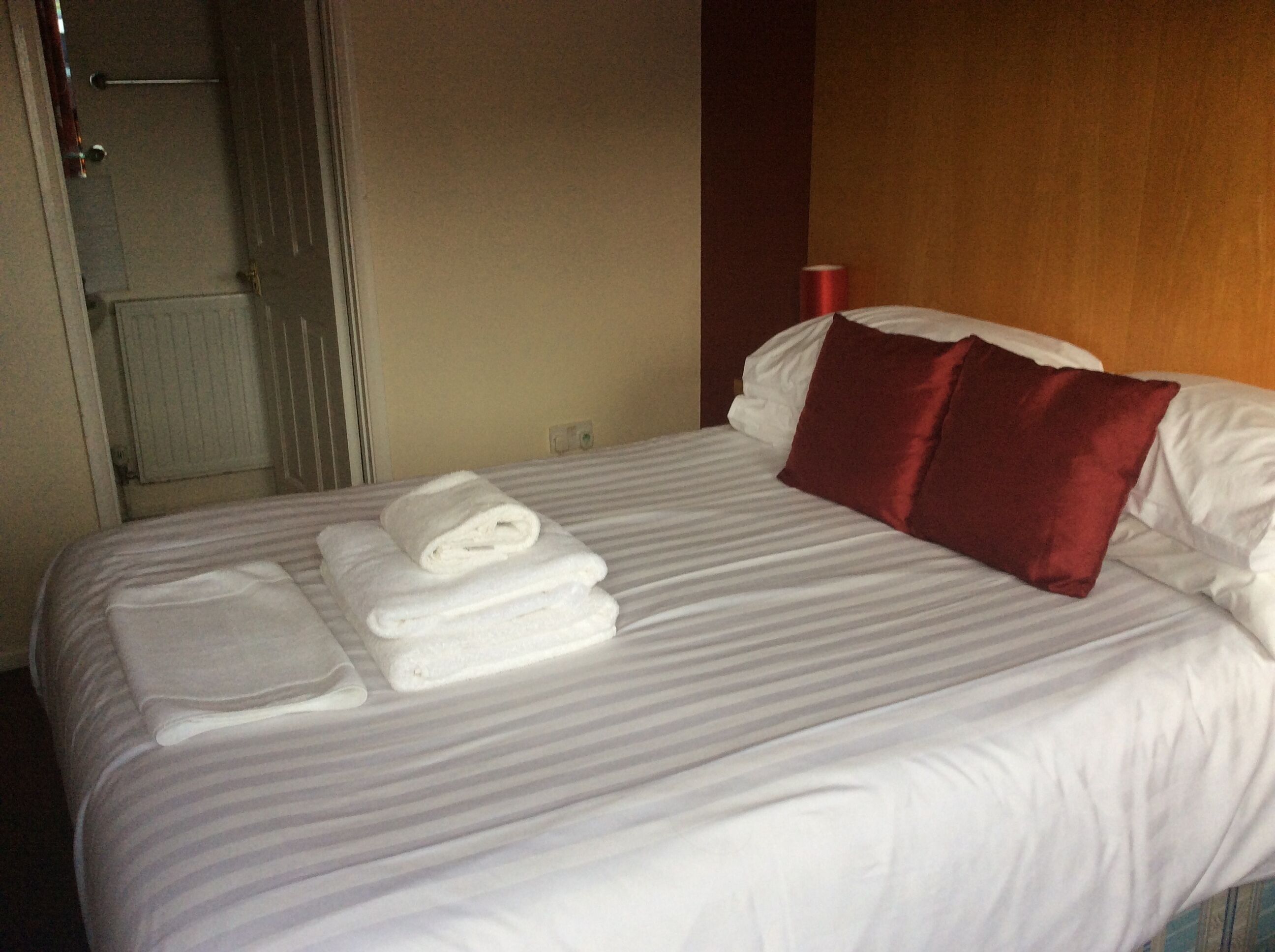 Una habitación de hotel con una cama bien hecha, una almohada roja y una toalla doblada sobre la cama.