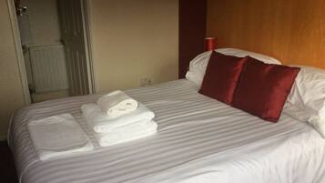 Una habitación de hotel con una cama bien hecha, una almohada roja y una toalla doblada sobre la cama.
