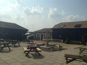 An outdoor courtyard with picnic tables, a fountain, and stone buildings. - Coach House Hotel (Royston)