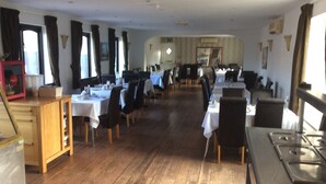 A restaurant with wooden floors, tables with white tablecloths, and black chairs. - Coach House Hotel (Royston)