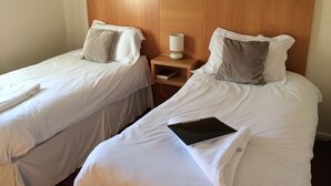 A hotel room with two single beds, each with white linens and pillows. There is a bedside table with a lamp and a book. - Coach House Hotel (Royston)