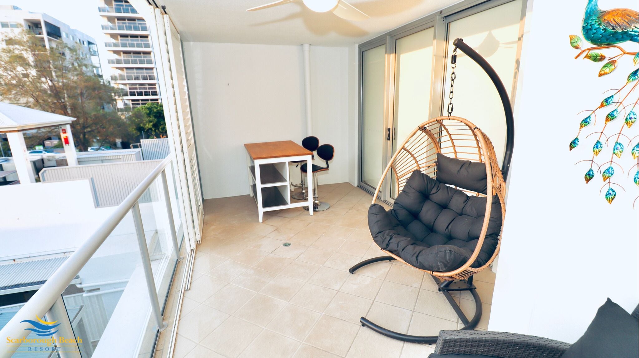 A balcony with a hanging chair, a small table with two chairs, and a view of buildings.