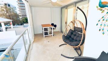 A balcony with a hanging chair, a small table with two chairs, and a view of buildings.