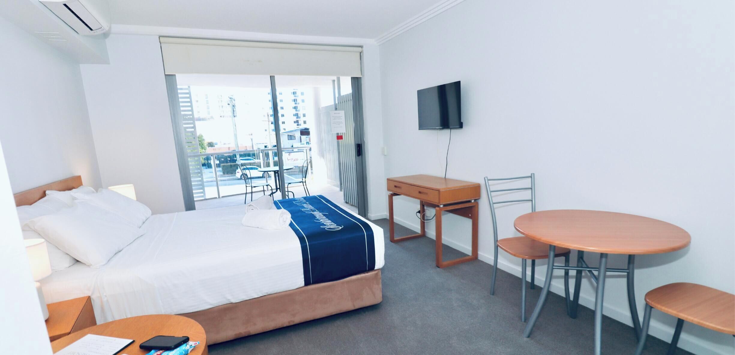 A hotel room with a bed, a desk, a chair, a TV, and a balcony view.