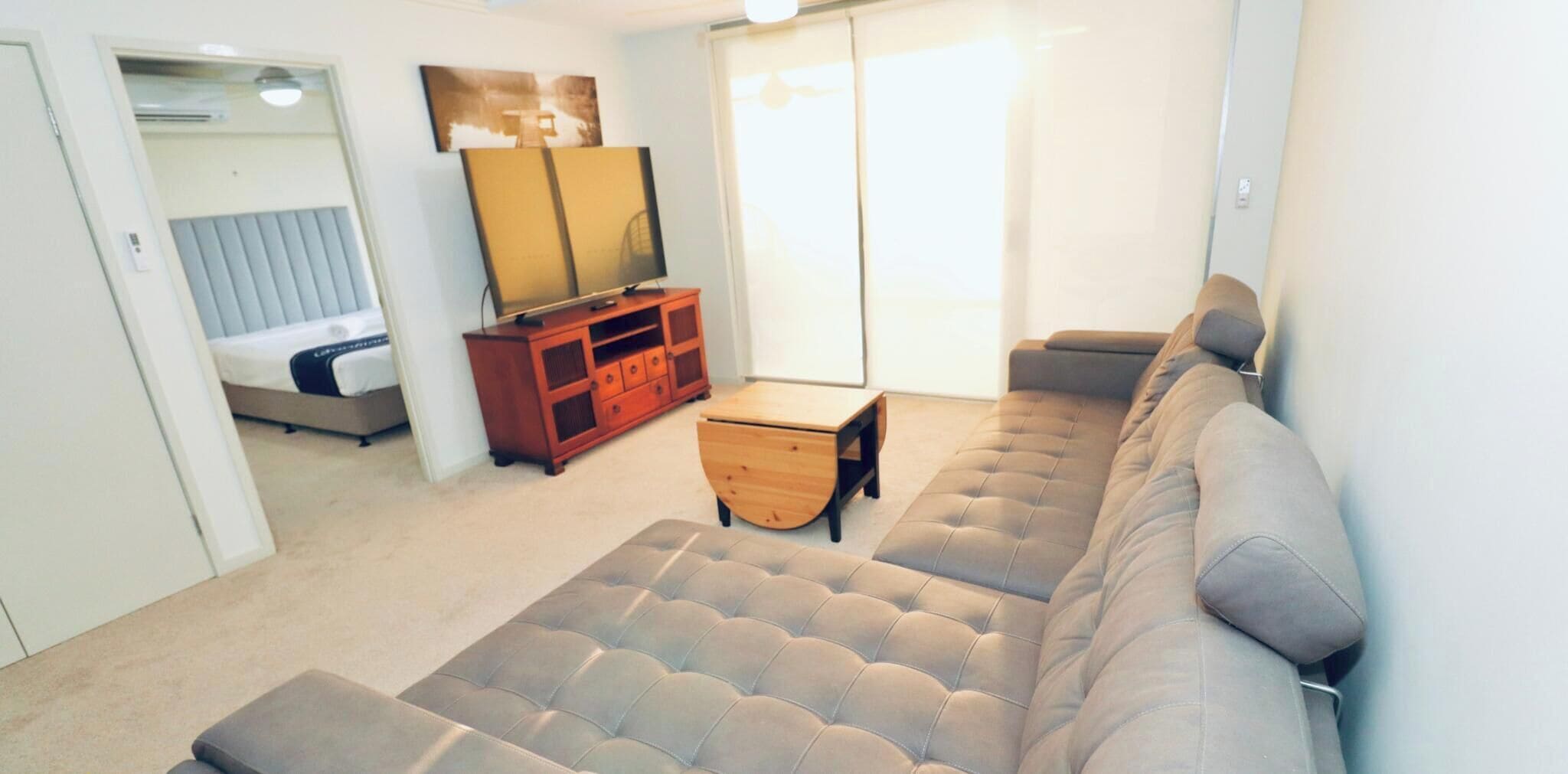 A living room with a sofa, a wooden cabinet, a small table, and a bed.
