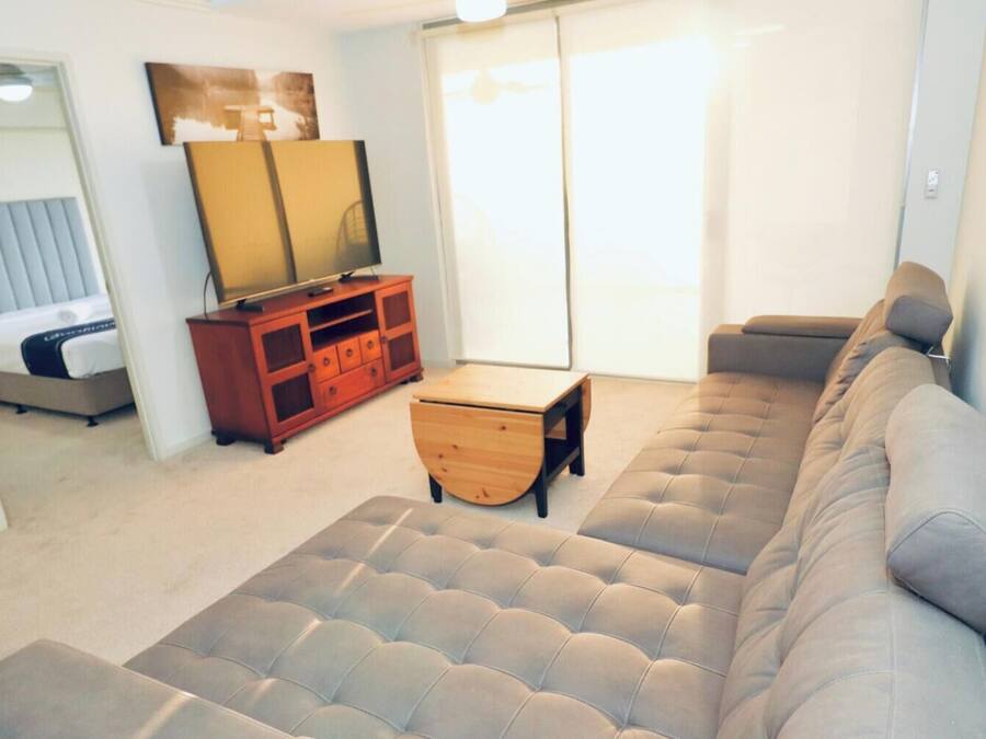 A living room with a sofa, a wooden cabinet, a small table, and a bed.