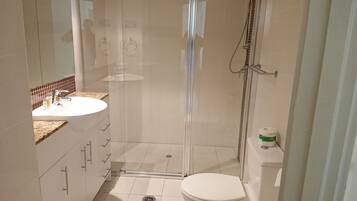 Un baño moderno con ducha de vidrio, lavamanos blanco y retrete.