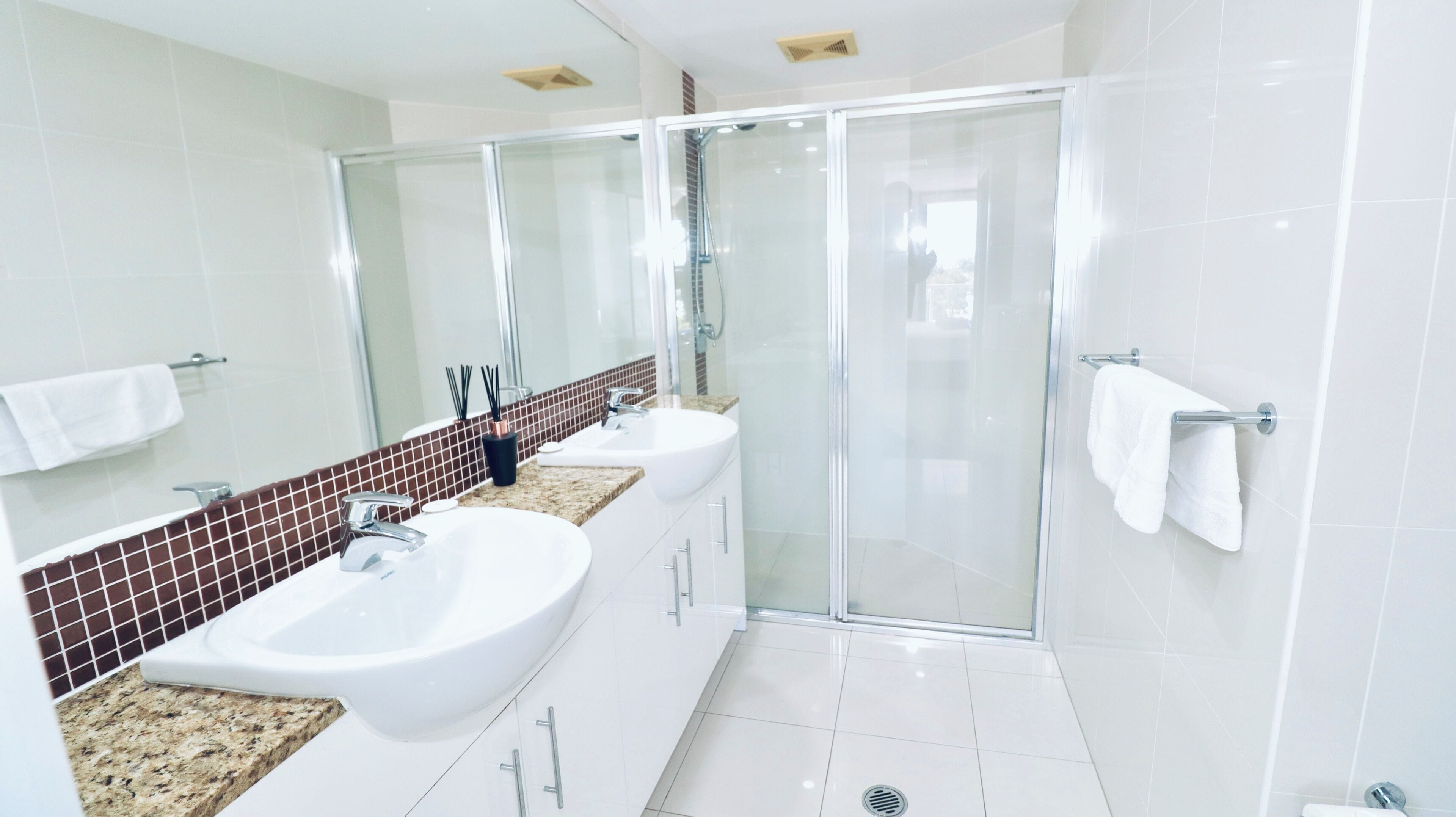 A modern bathroom with two sinks, a glass shower enclosure, and a large mirror.