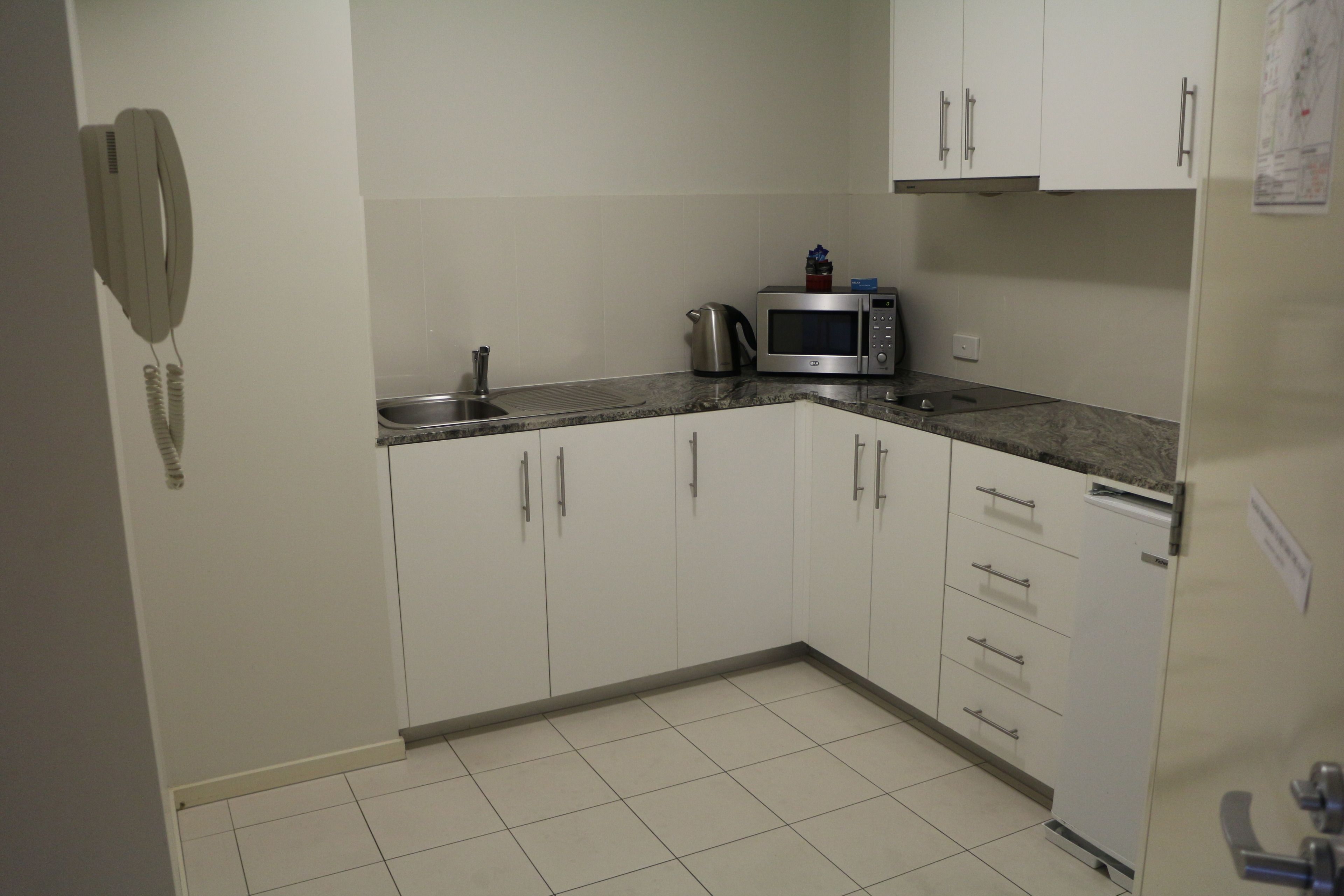 A kitchen with white cabinets, a microwave, a kettle, and a telephone.