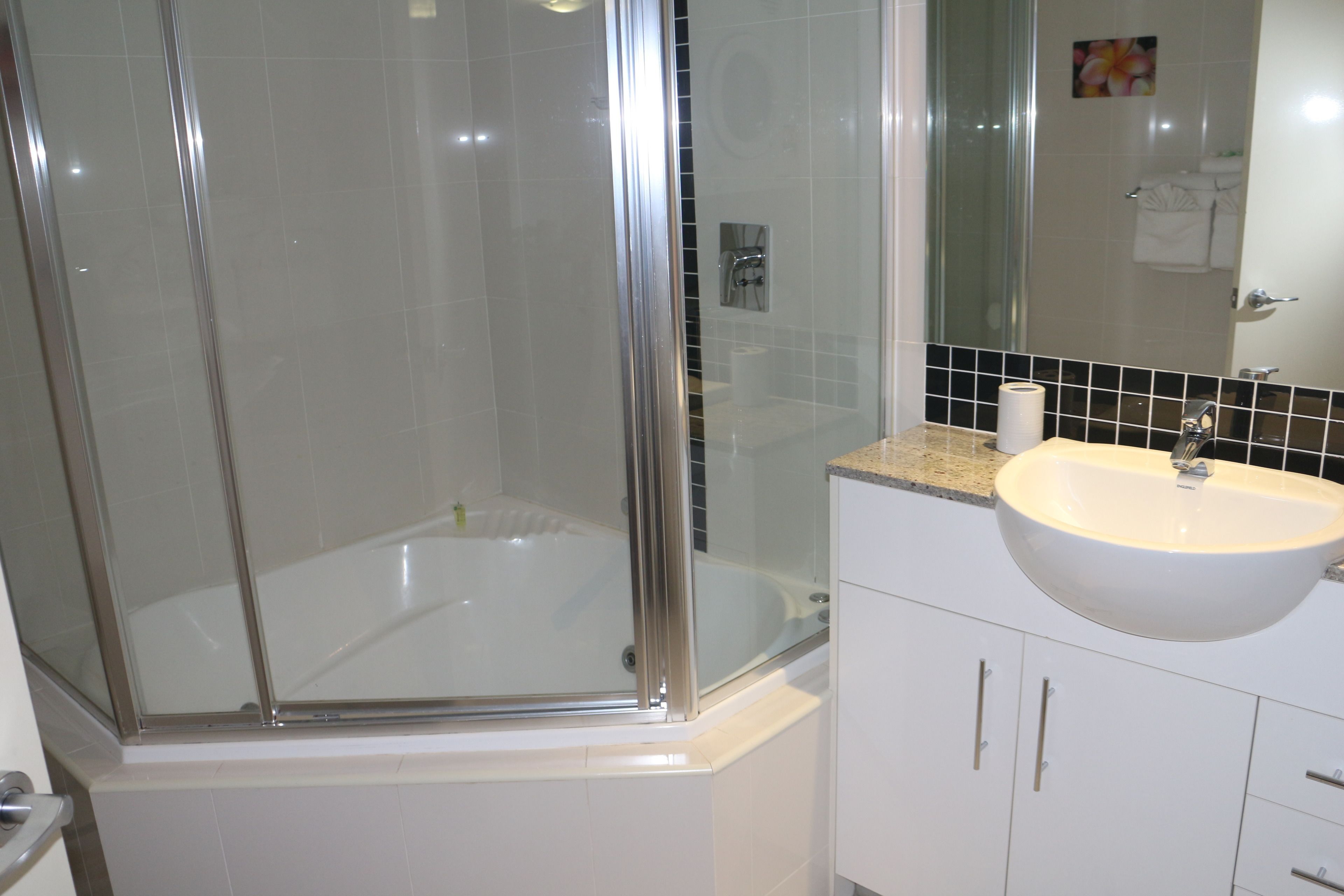 A modern bathroom with a glass-enclosed shower, a white sink, and a tiled wall.