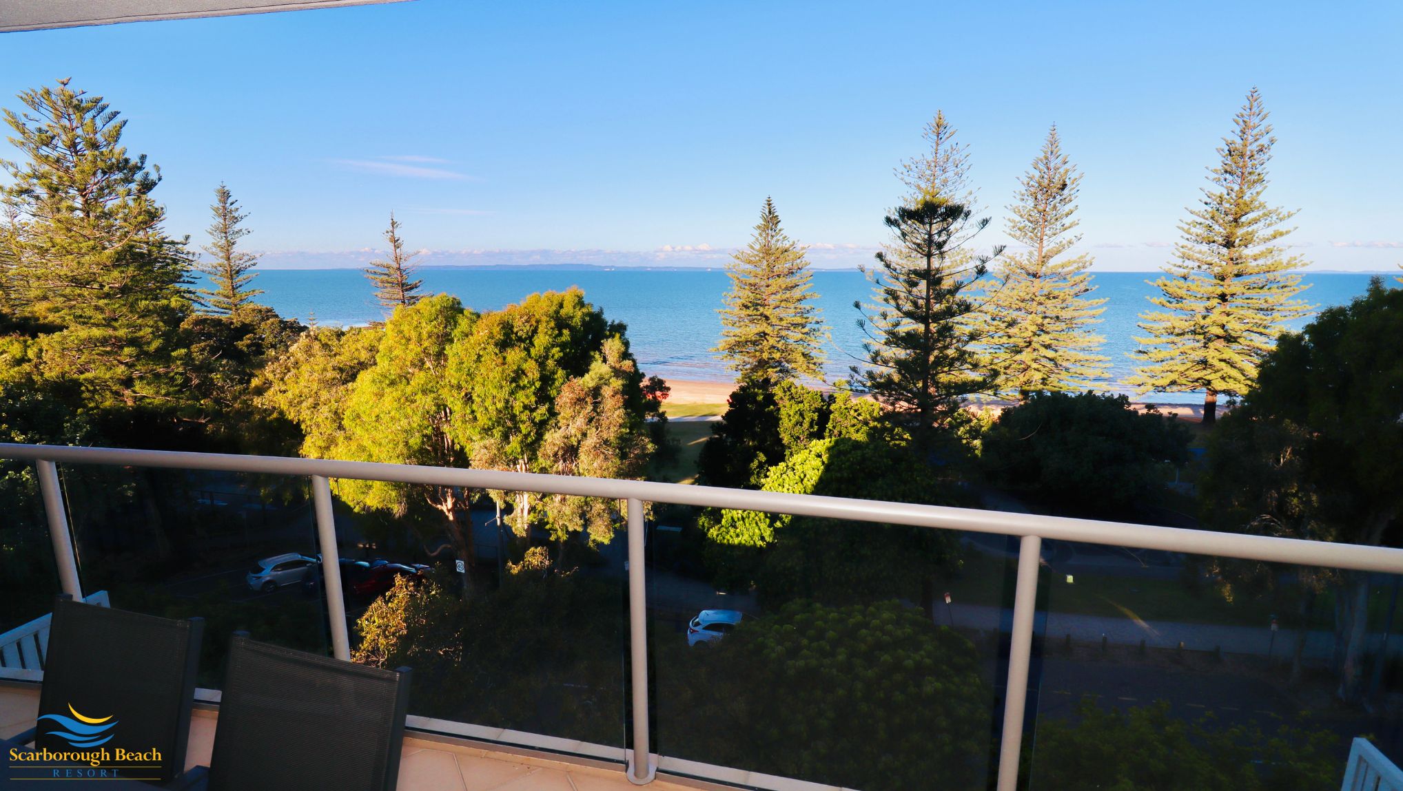 A balcony with a clear view of the ocean, trees, and a distant beach.