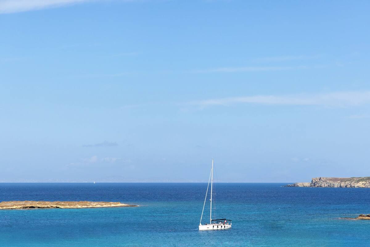 A sailboat on a calm sea with a rocky coastline in the background.