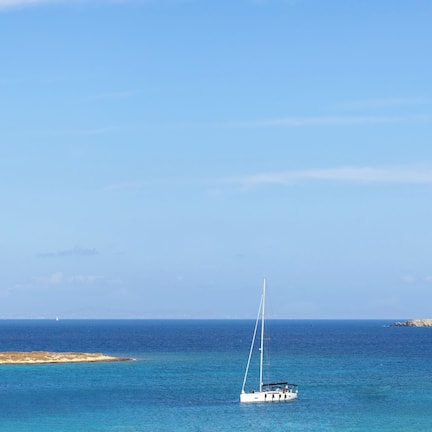 A sailboat on a calm sea with a rocky coastline in the background.