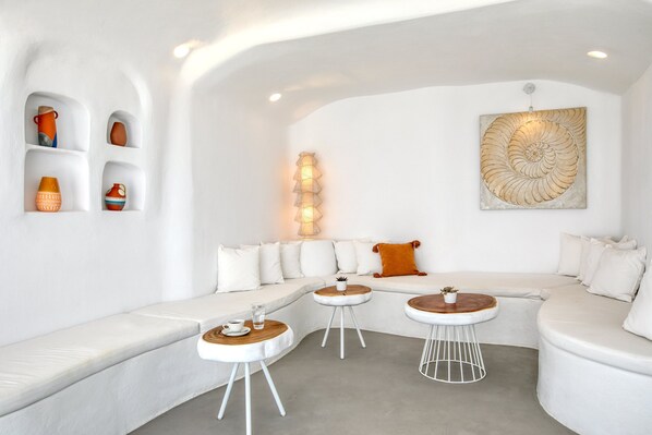 A modern living room with a white sofa, two round tables, and decorative pottery on shelves. - Lilly Residence-All Sea View Suites | Adults Only (Paros)