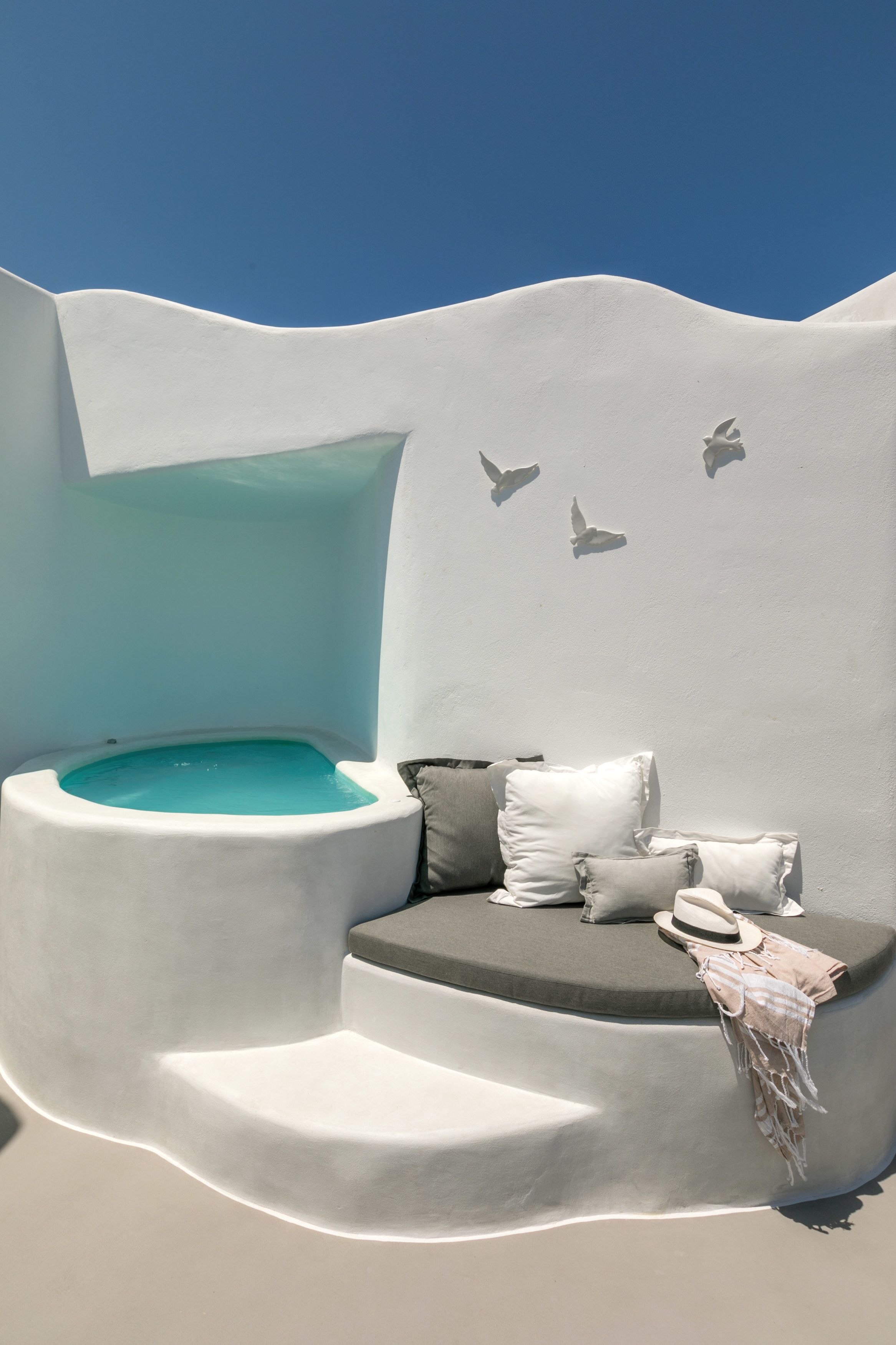 A modern, minimalist room with a built-in bathtub, a cushioned seating area, and a wall-mounted bird sculpture.