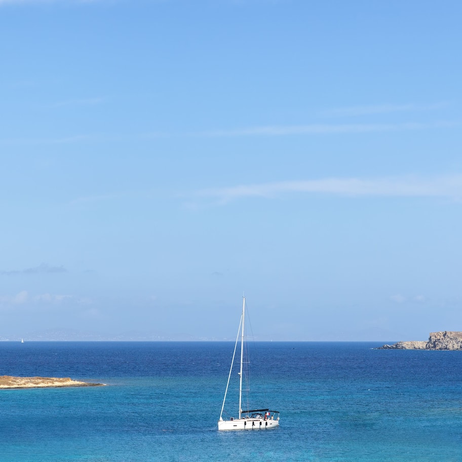 A sailboat on a calm sea with a rocky coastline in the background.