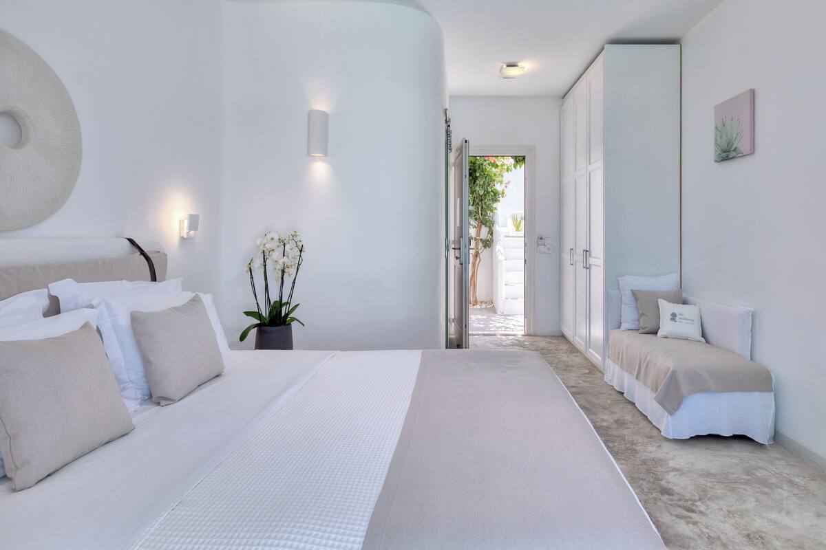 A modern bedroom with a large bed, bedside tables, a potted plant, and a view of the outside.