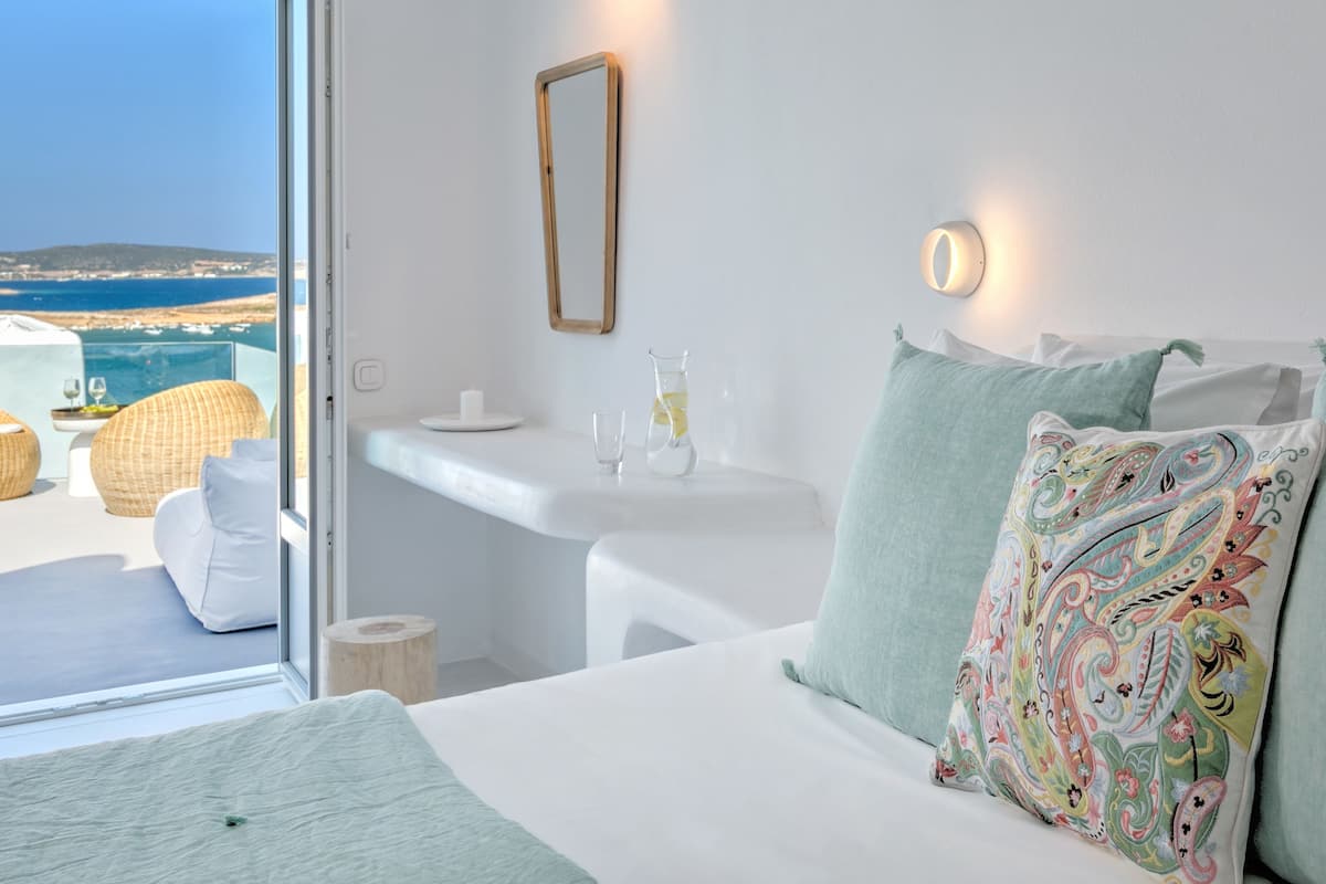 A hotel room with a bed, a bedside table, a mirror, and a view of the sea.