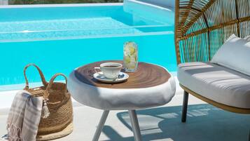 A poolside setting with a wicker chair, a small round table with a cup and a glass, and a woven bag.