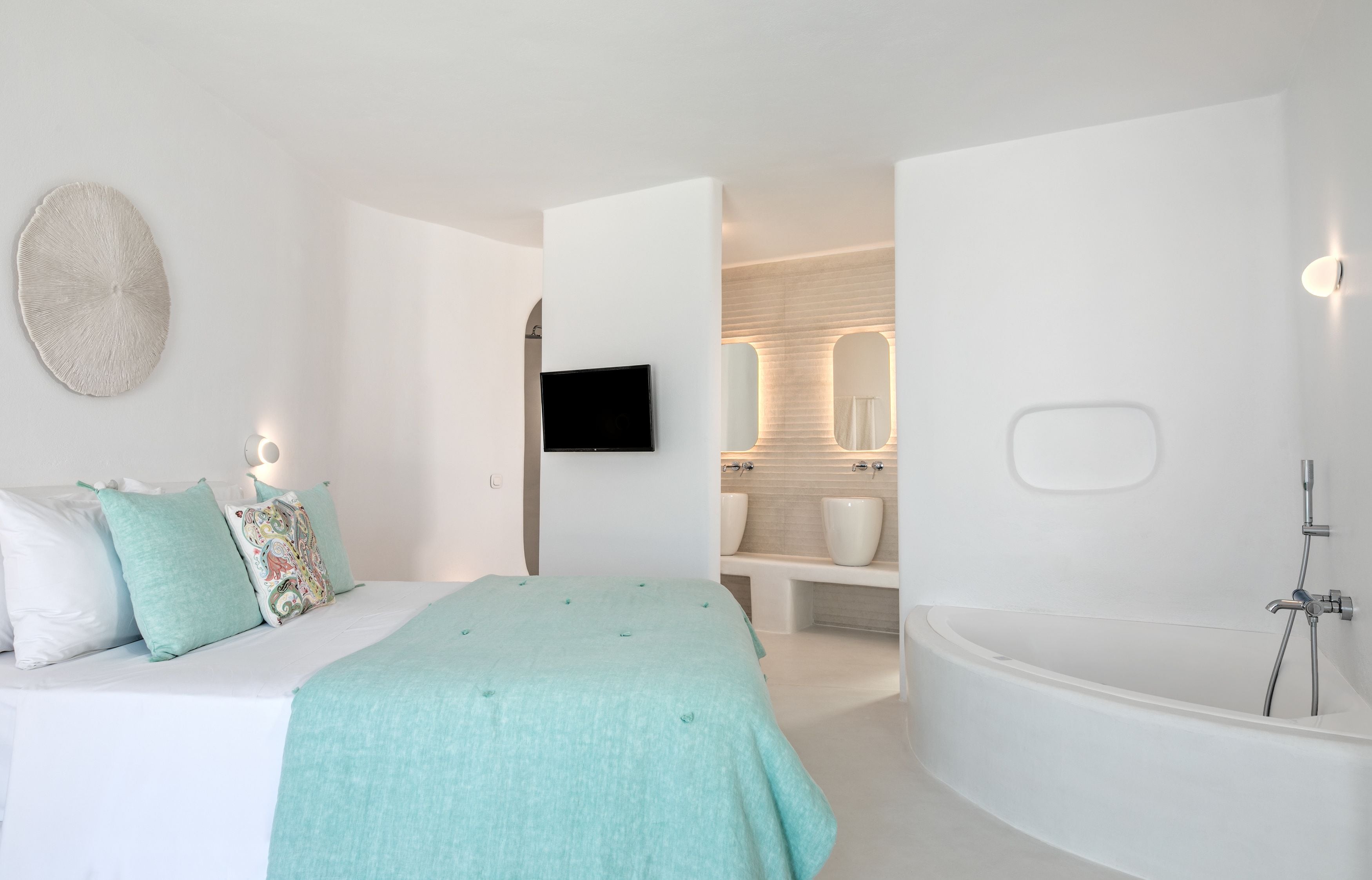 A modern bedroom with a bed, a large mirror, a flat-screen TV, and a bathroom with a bathtub and sink.