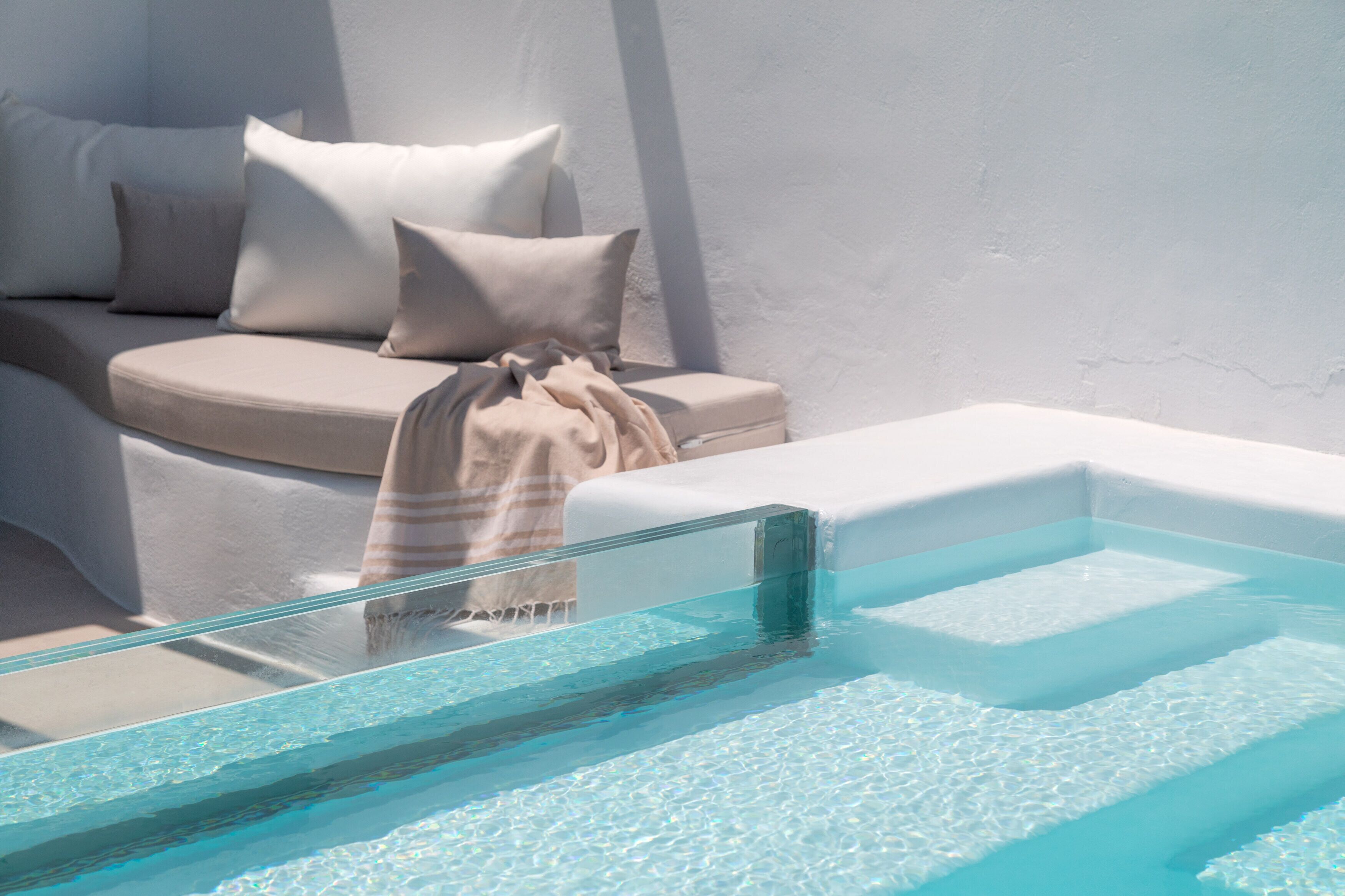 A modern spa area with a glass-enclosed pool, a beige sofa with cushions, and a white wall.