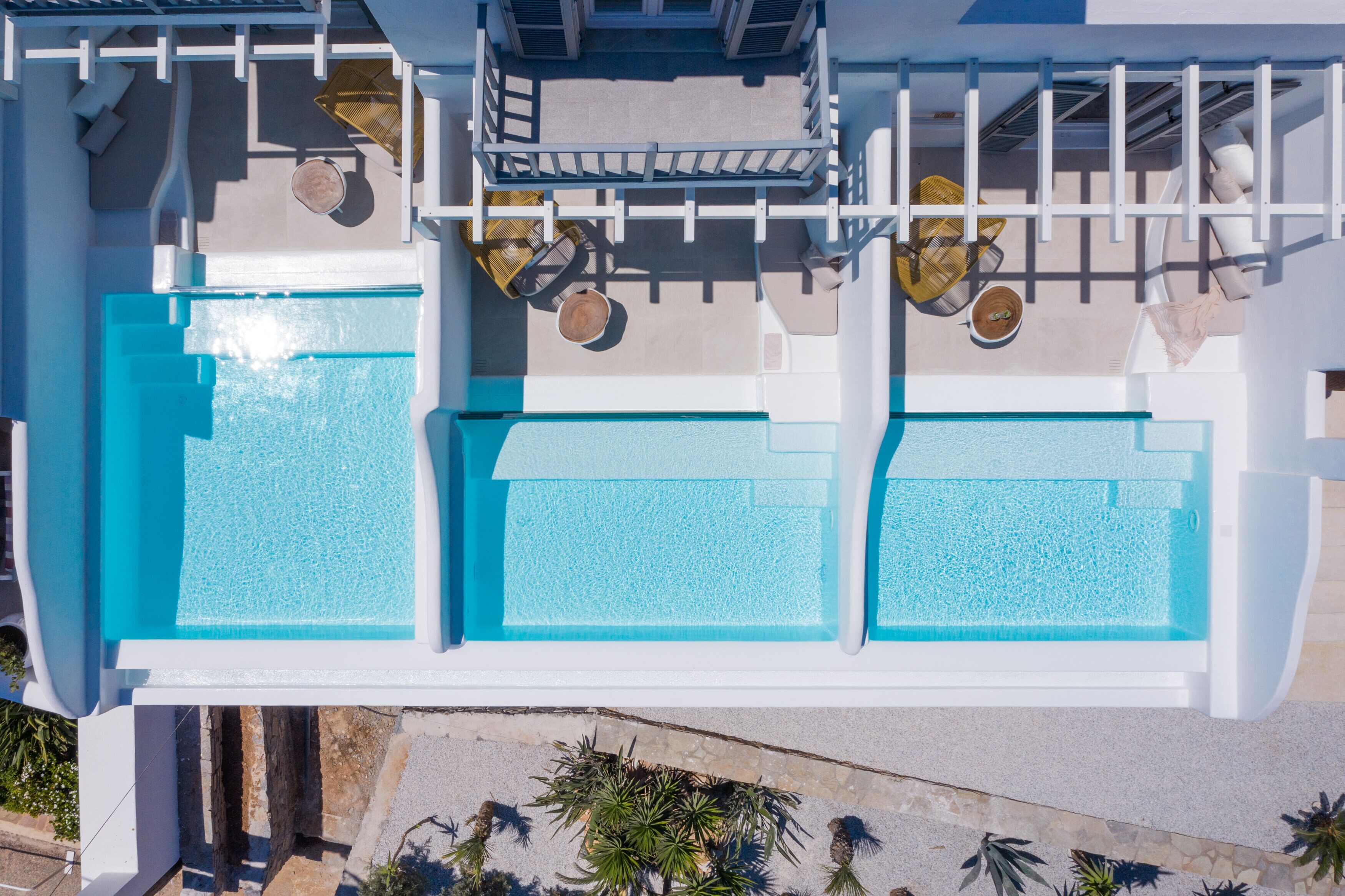 An aerial view of a hotel with three swimming pools, a covered seating area with tables and chairs, and a stone pathway leading to the pool.