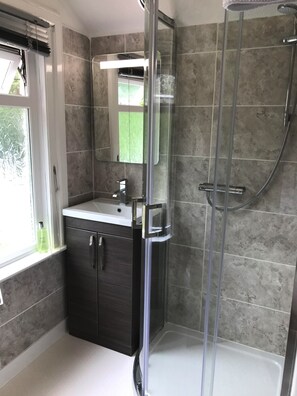 A modern bathroom with a glass shower enclosure, a sink with a mirror, and a window with blinds. - Cornerways (Ventnor)