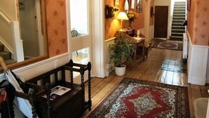 A hallway with wooden flooring, a patterned rug, a desk with a lamp, and a staircase.