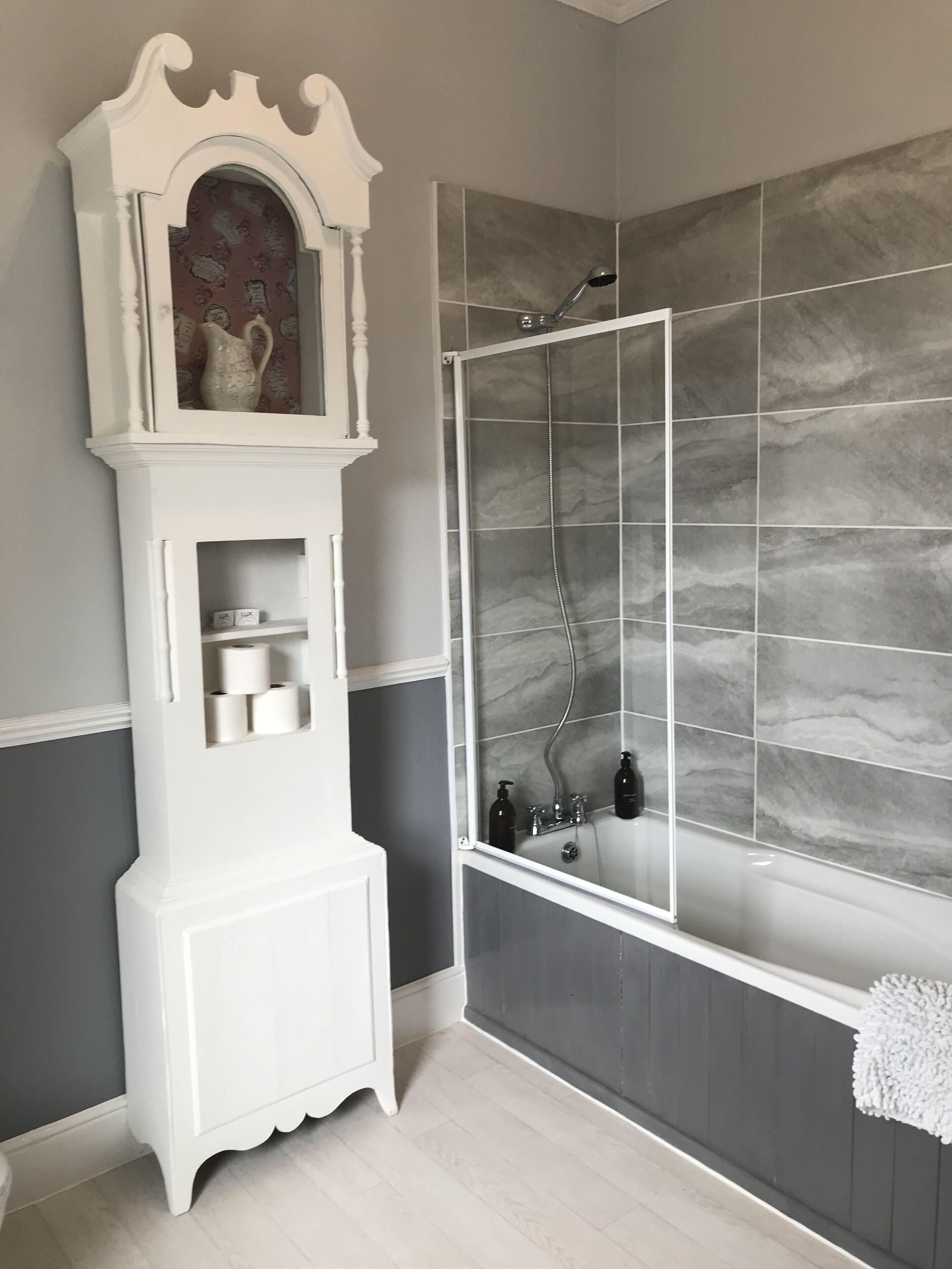 A bathroom with a white vanity, a shower with grey tiles, and a mirror.