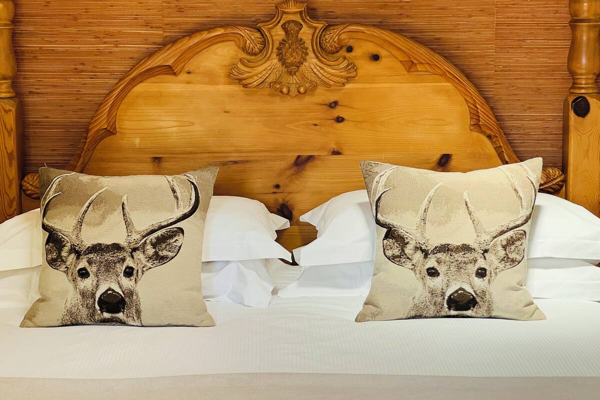 A bed with two pillows featuring a deer design, a wooden headboard, and white bedding.