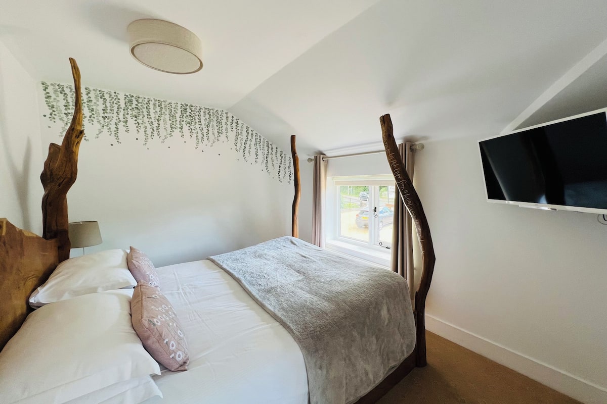 A bedroom with a bed, a television mounted on the wall, and a window with curtains.