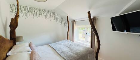 Un dormitorio con cama, televisor montado en la pared y ventana con cortinas.
