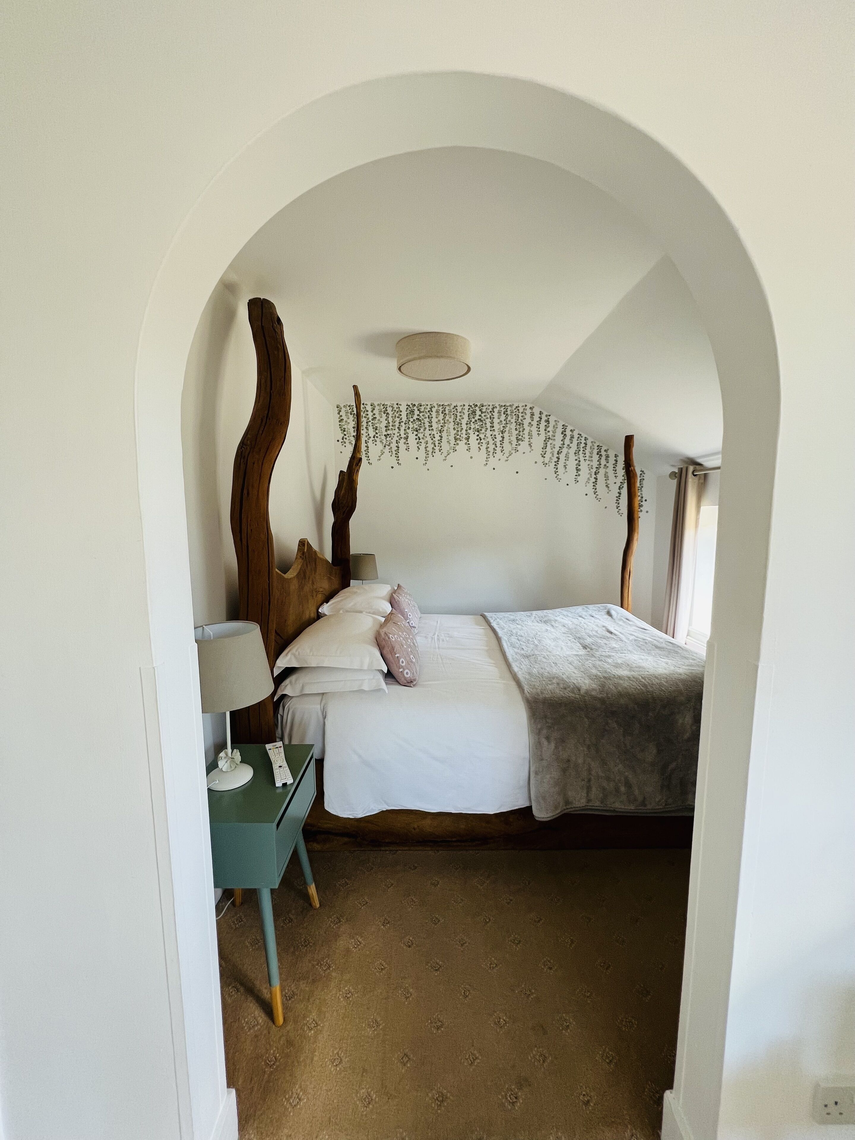 A bedroom with a bed, a desk, and a hanging plant.