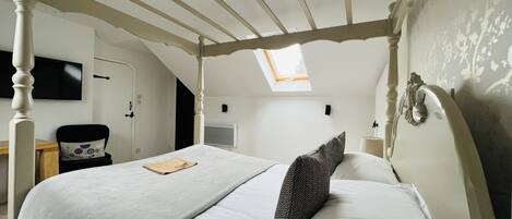 Un dormitorio con cama con dosel, tragaluz, televisión de pantalla plana y un pequeño escritorio con silla.