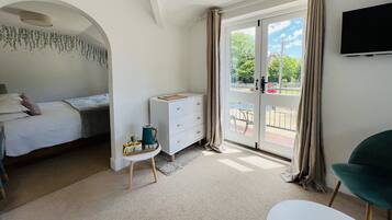 A bedroom with a bed, a dresser, a small table with items, and a view through a glass door to an outdoor area.