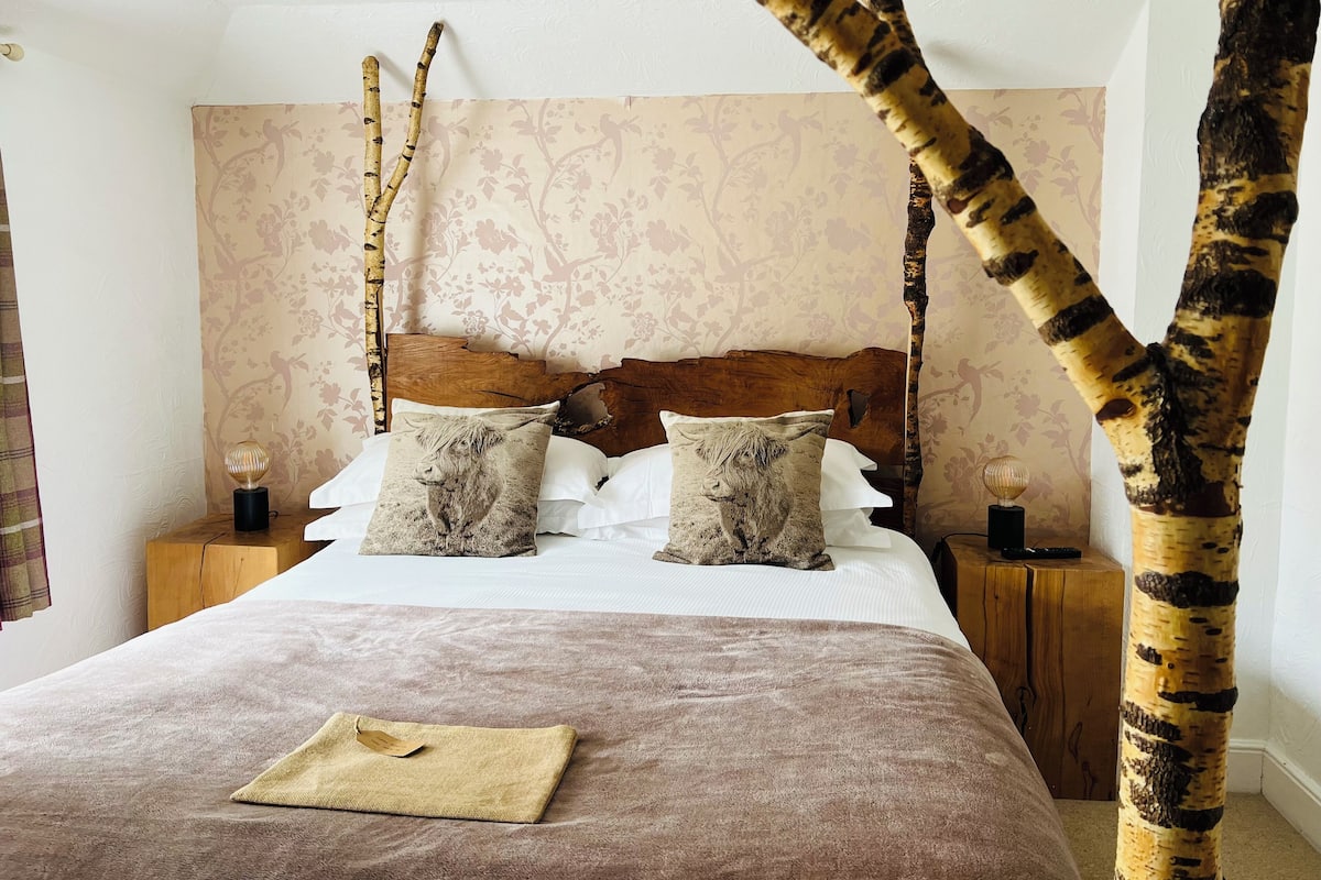 A bedroom with a four-poster bed, two nightstands, and a decorative tree branch.