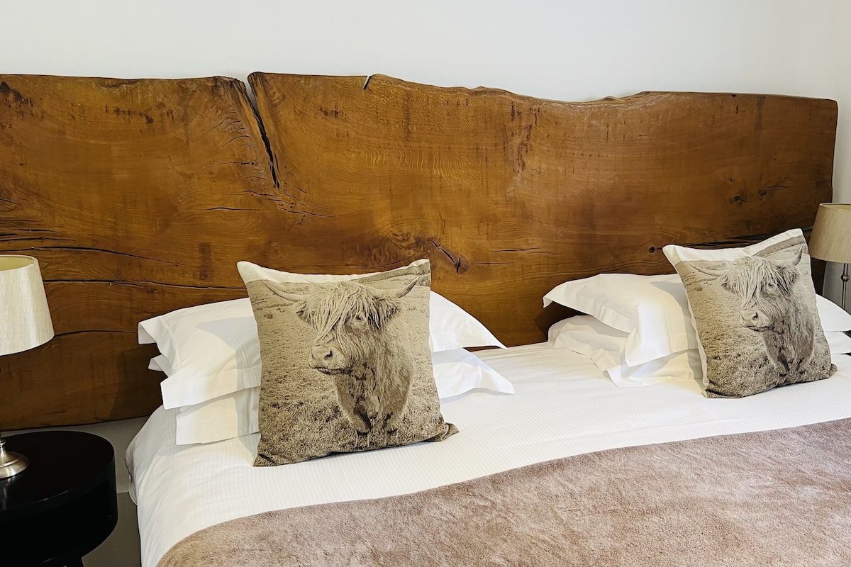 A bed with a wooden headboard, two decorative pillows, white bedding, and a nightstand with a lamp.