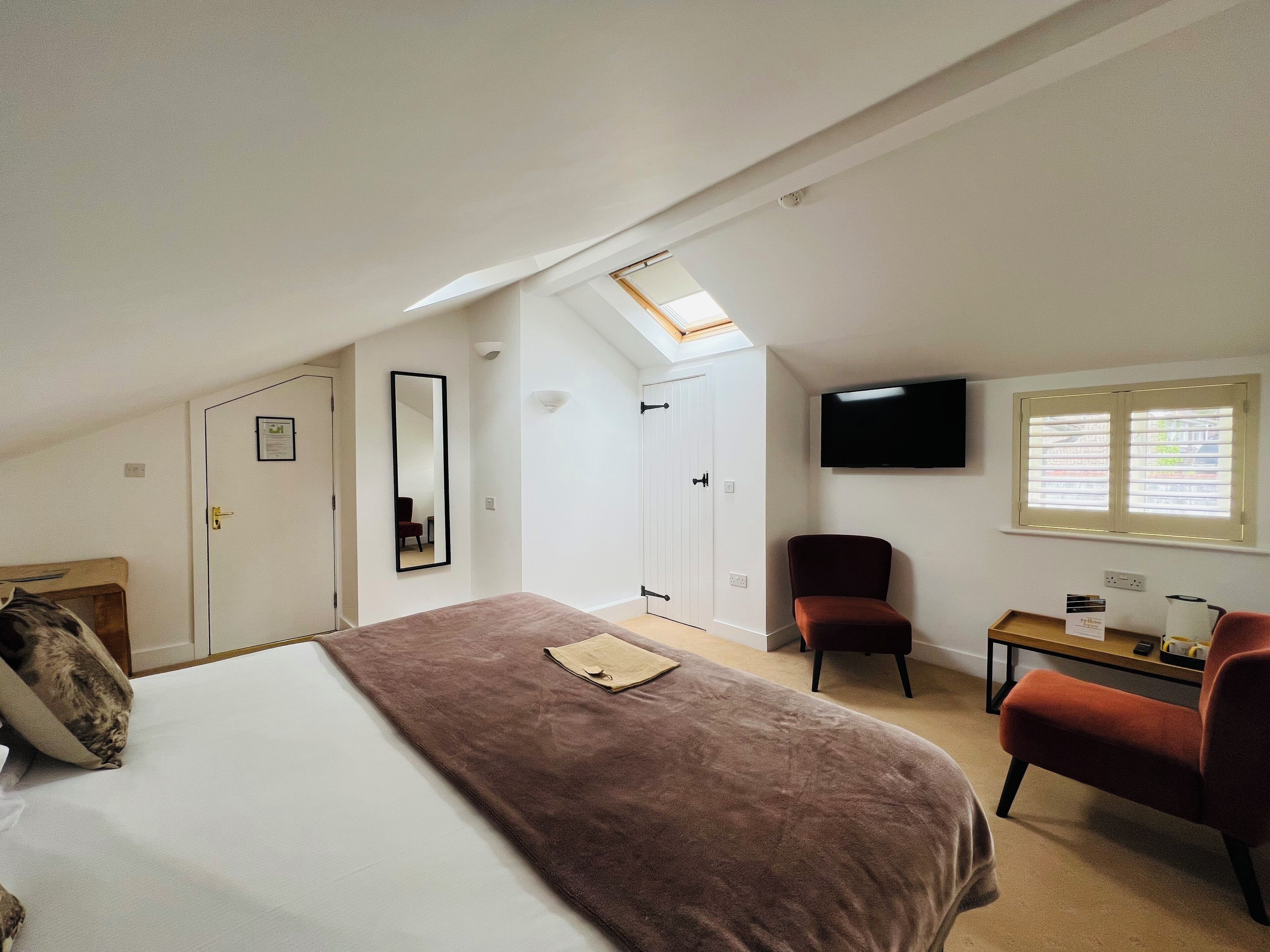 A bedroom with a large bed, a desk, a chair, a TV, and a window.