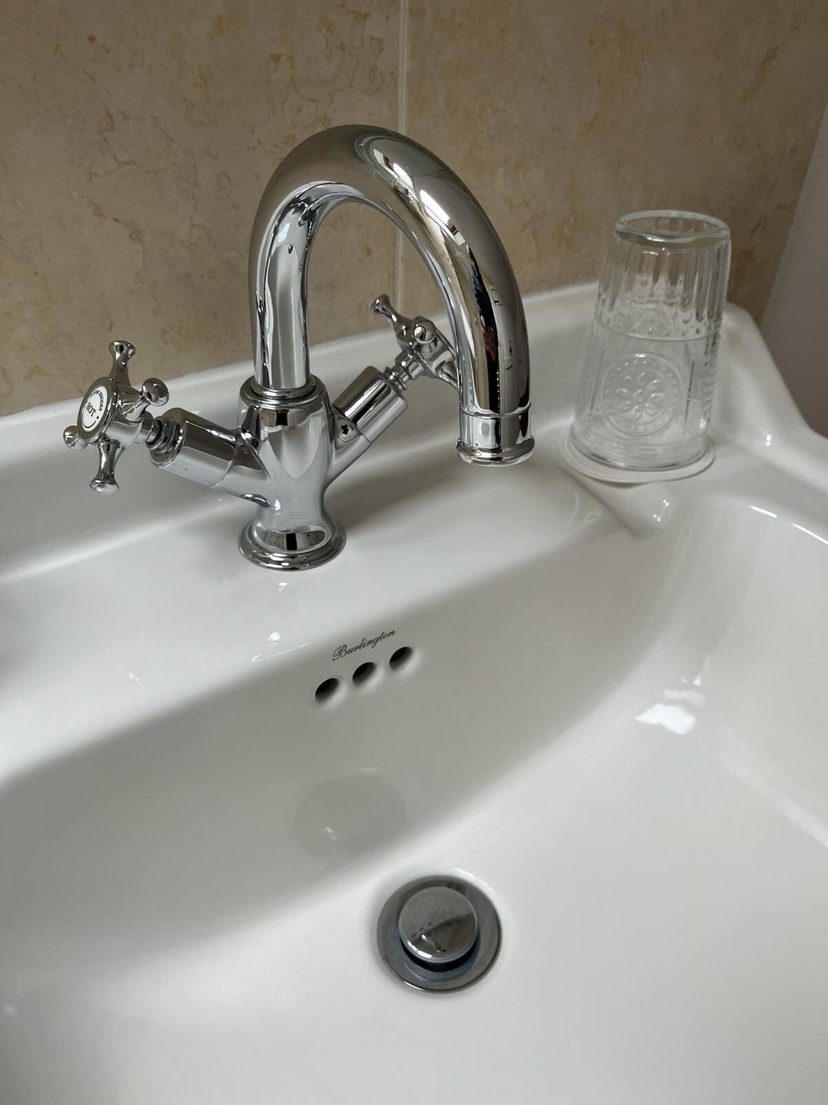 A bathroom sink with a chrome faucet, a clear glass, and a drain.