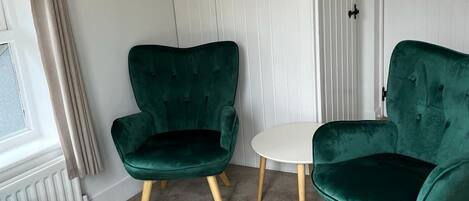 A room with two green velvet chairs, a small round table, and a matching ottoman.