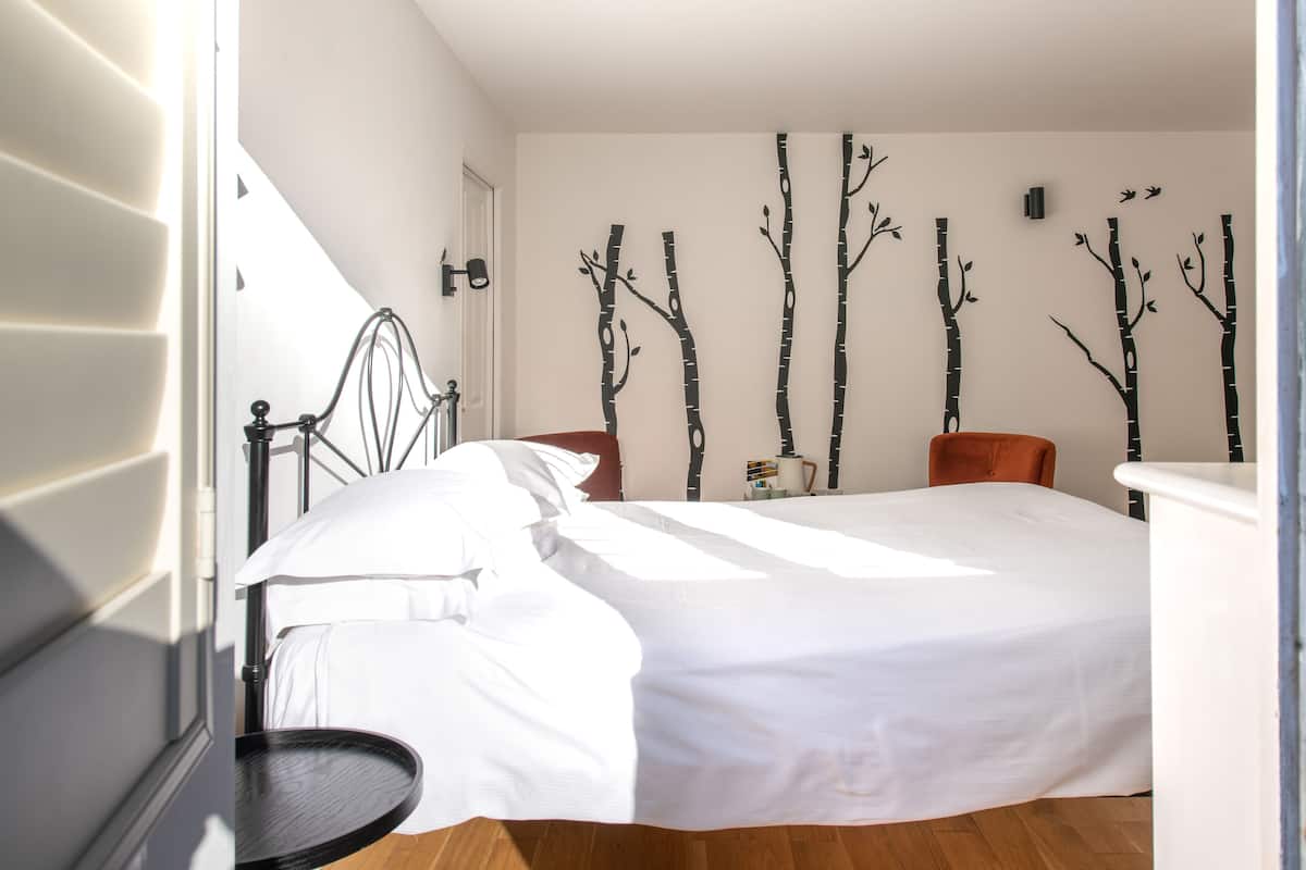 A bedroom with a bed, a chair, a small table, and a wall with tree decorations.