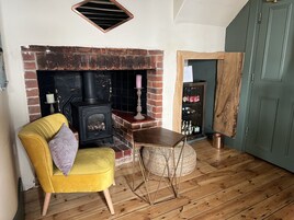 A cozy room with a brick fireplace, a yellow armchair, a small wooden table, and a woven pouf.