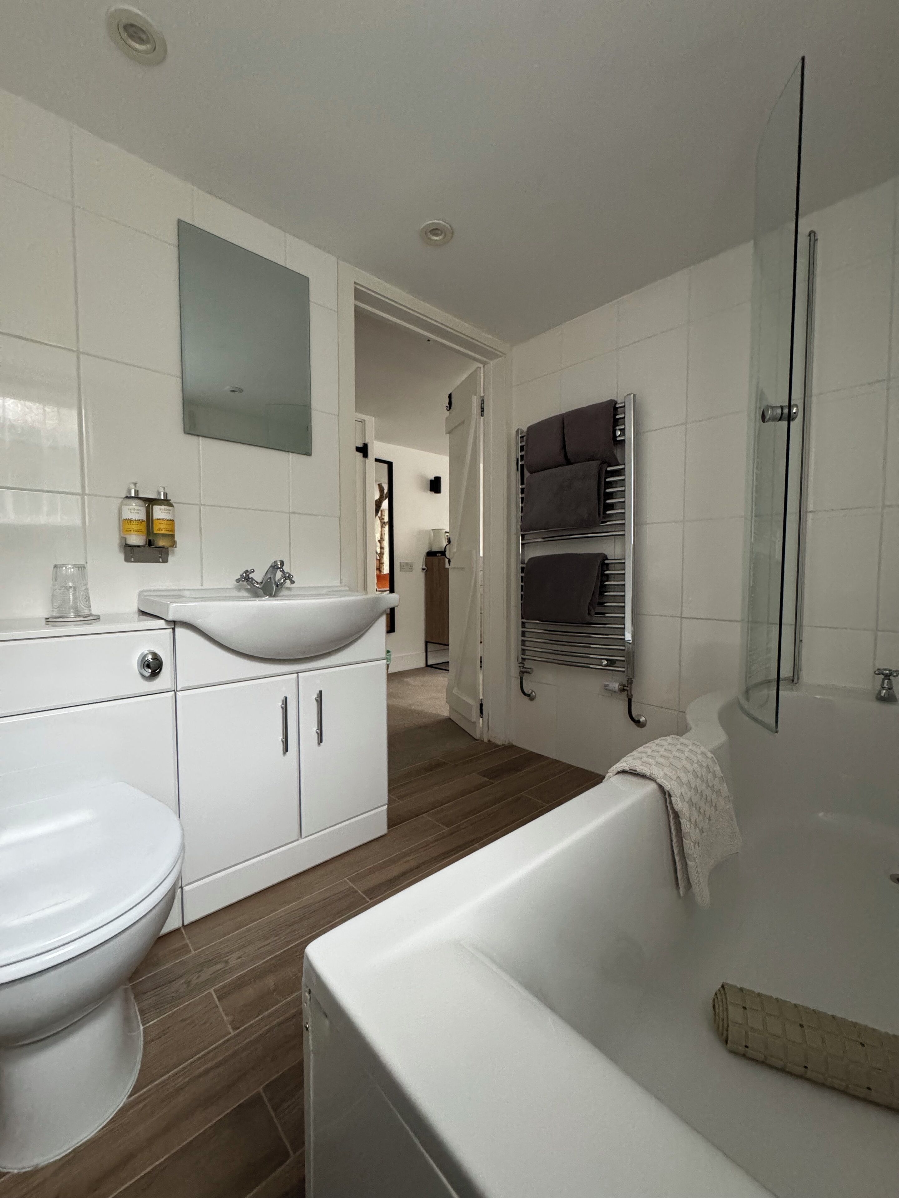 Une salle de bain moderne avec un lavabo, des toilettes et une baignoire blancs. On y trouve une cabine de douche en verre et un porte-serviettes.