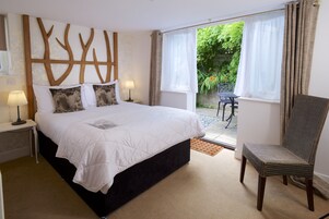 A bedroom with a large bed, a chair, a nightstand with a lamp, and a view of the garden through the window.