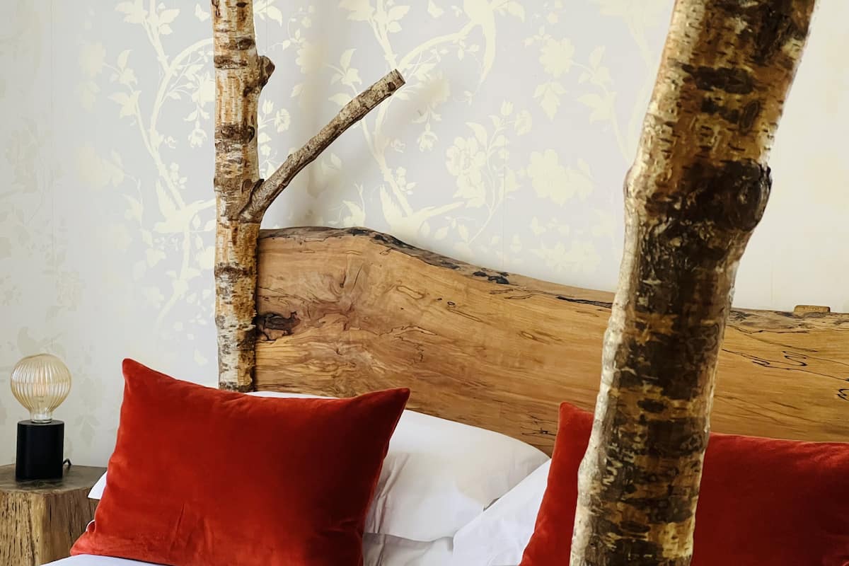 A bed with a wooden headboard, red pillows, and a nightstand with a lamp.