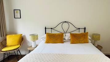 Un lit bien fait, avec une literie blanche et deux oreillers jaunes, une chaise en osier avec un coussin jaune, et deux lampes de chevet avec des abat-jour jaunes.