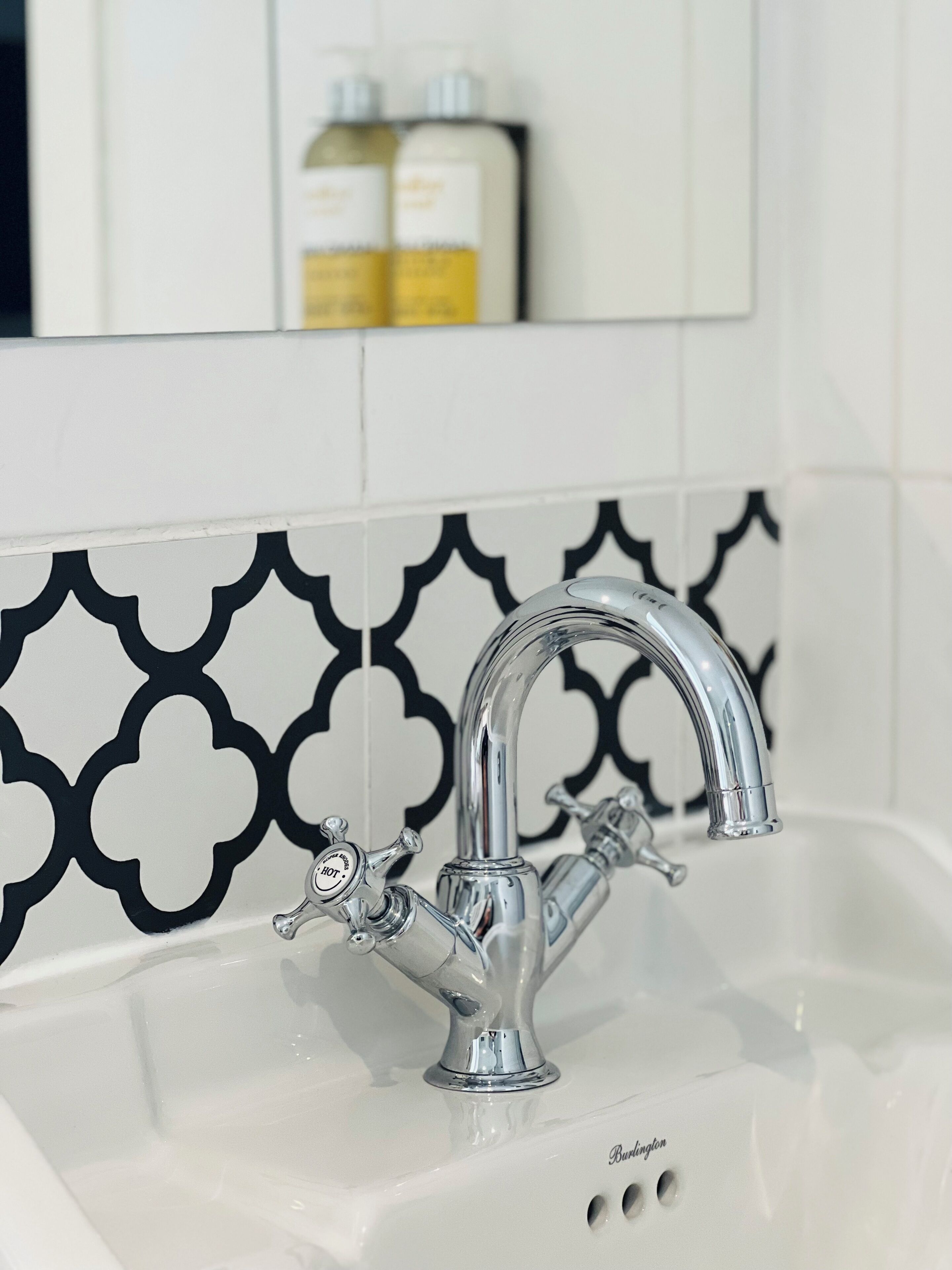 A bathroom sink with a modern faucet, a mirror above it, and a decorative black and white tile backsplash.