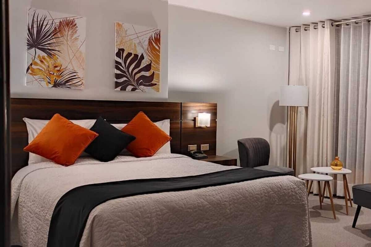 A hotel room with a bed, a desk, a chair, and a lamp.