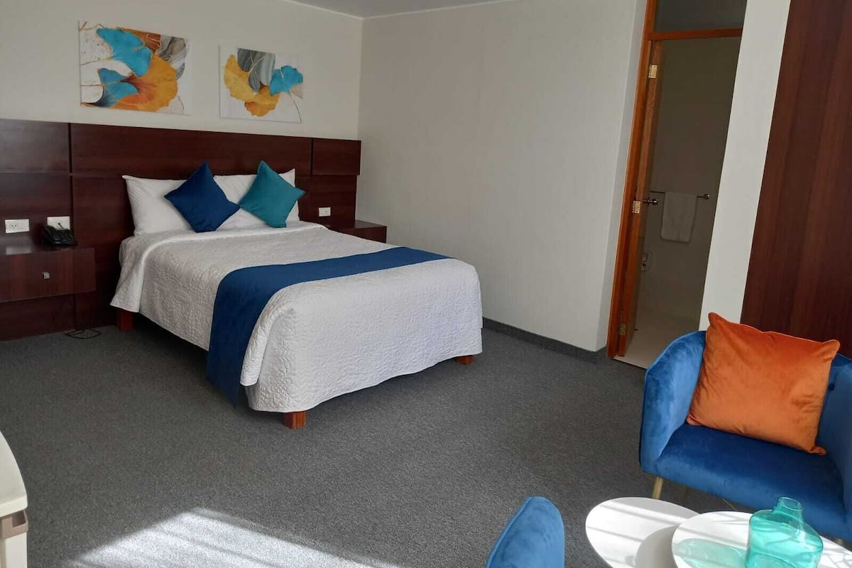 A hotel room with a bed, a nightstand, a chair, and a table.