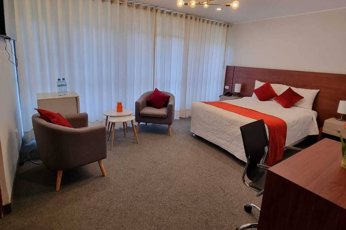 A hotel room with a bed, two armchairs, a desk, and a small table.
